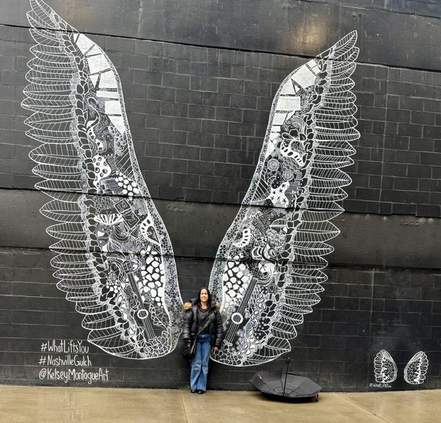 Mel standing in front of a mural of wings